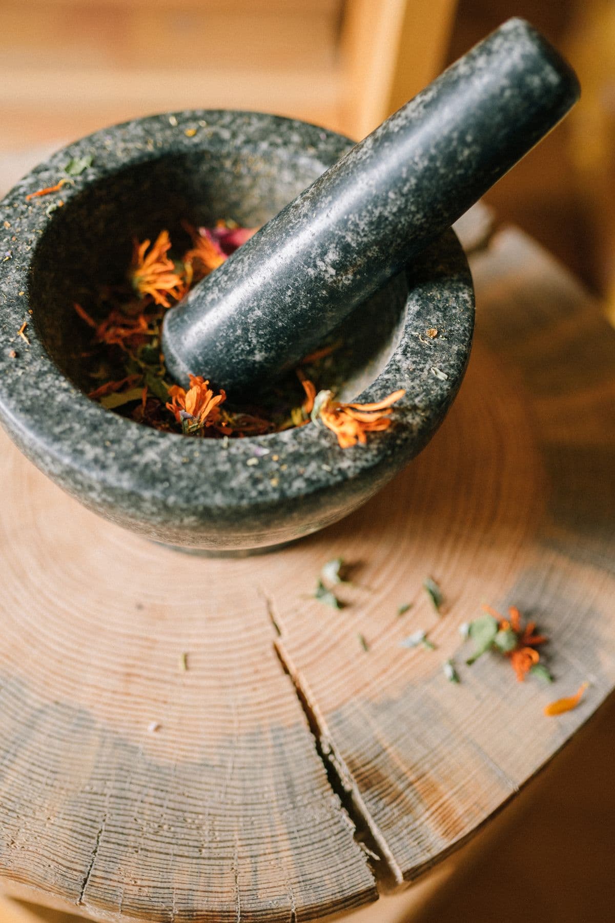 A stone mortar and pestle with dried botanicals and flower petals
