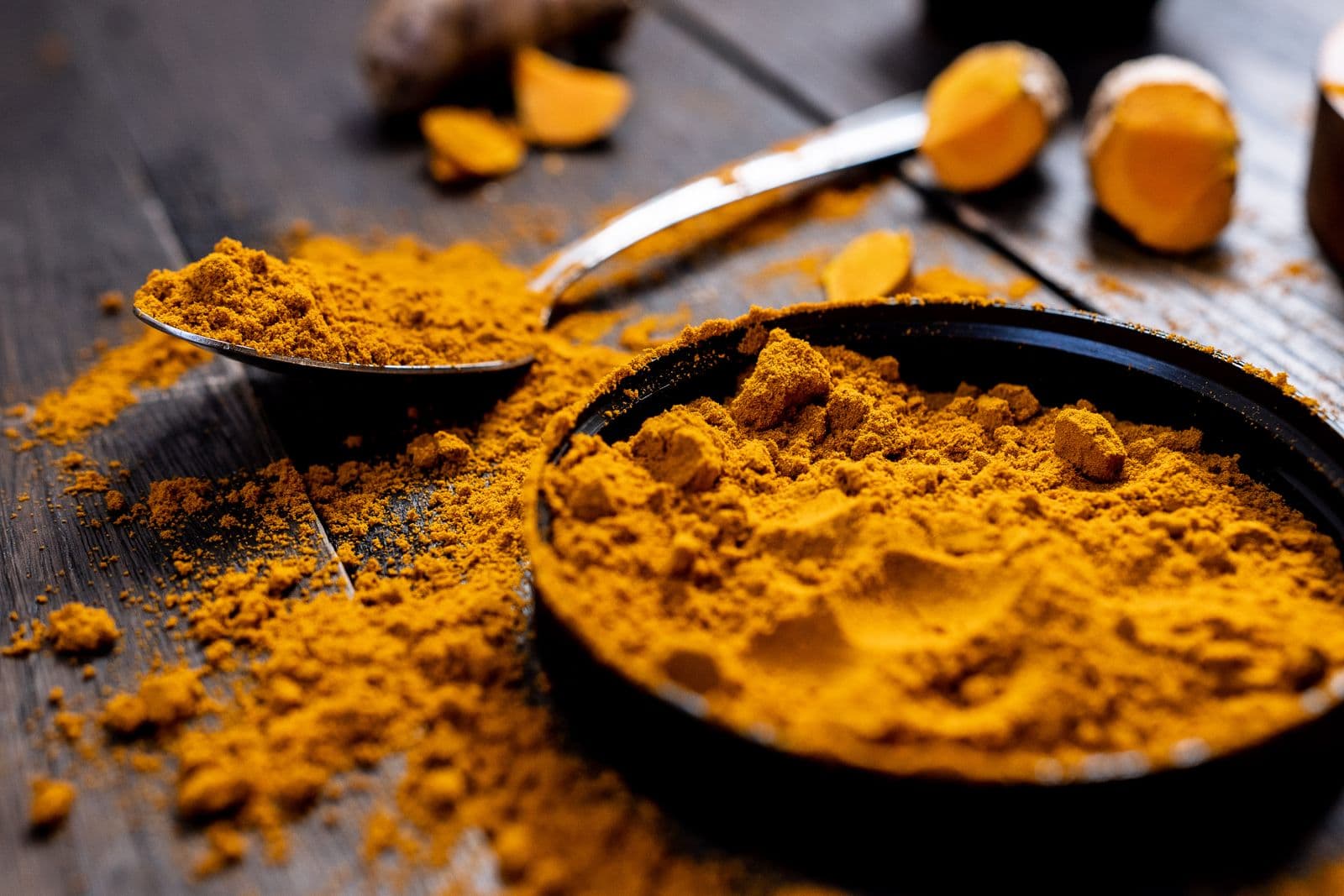 Golden turmeric powder with a spoon on a wooden surface